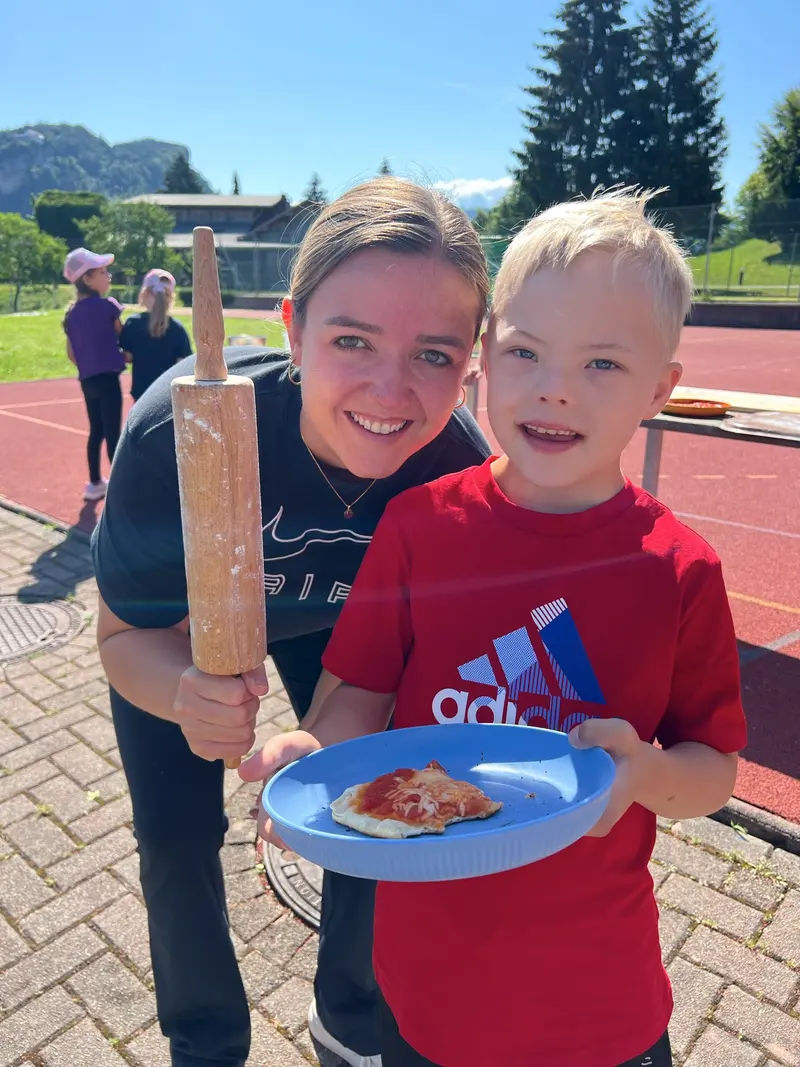 Betreuer und Kind posieren mit Nudelholz und Teller Essen