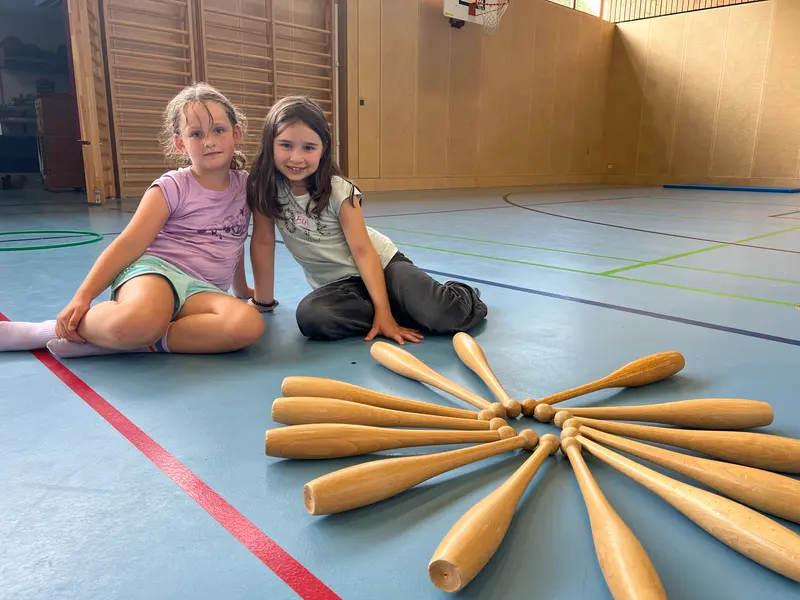 Zwei Kinder sitzen neben sternförmig angeordneten Holzkeulen