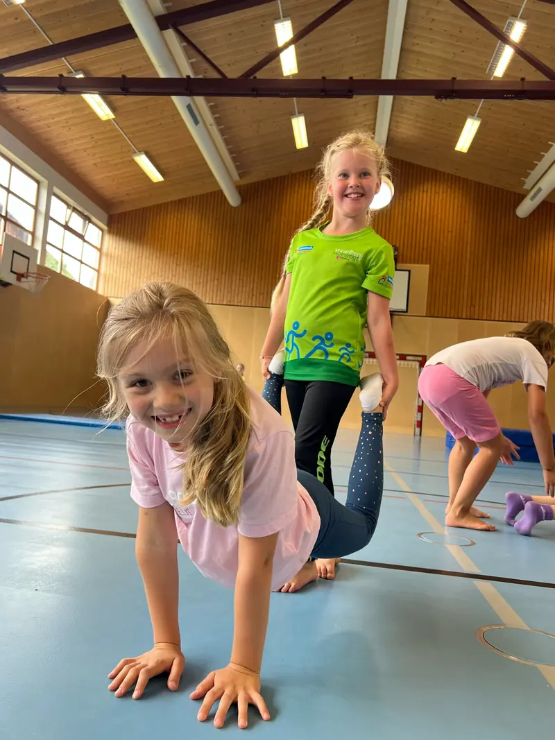 Kind übt eine Turnbewegung mit angehobenem Bein in der Halle