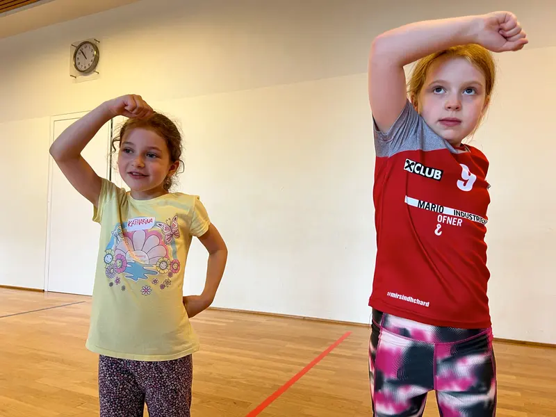 Zwei Kinder posieren mit erhobenem Arm in der Turnhalle
