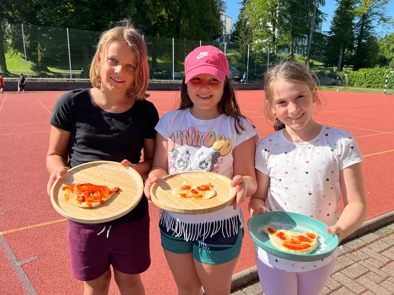 Drei Kinder halten lächelnd selbstgemachte Pizza in den Händen