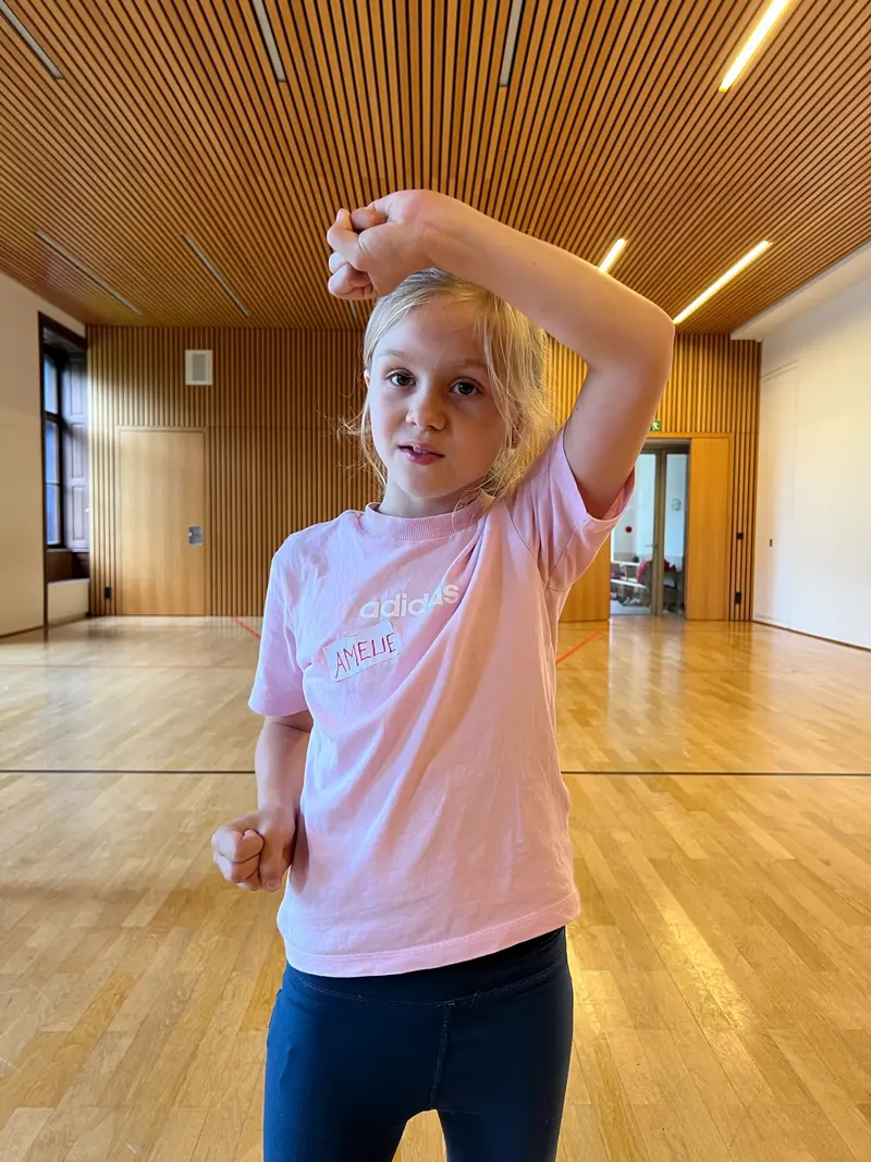 Kind tanzt mit erhobenem Arm in der Turnhalle