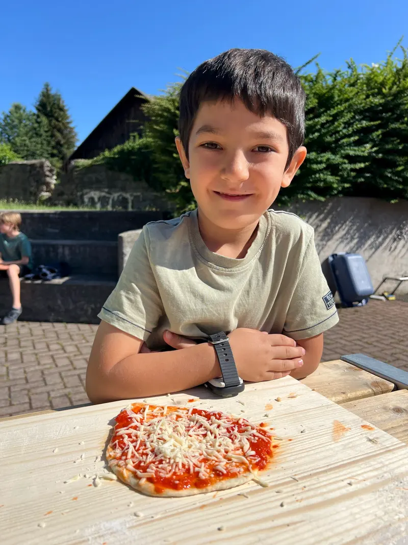Kind lehnt lächelnd mit verschränkten Armen an einem Tisch