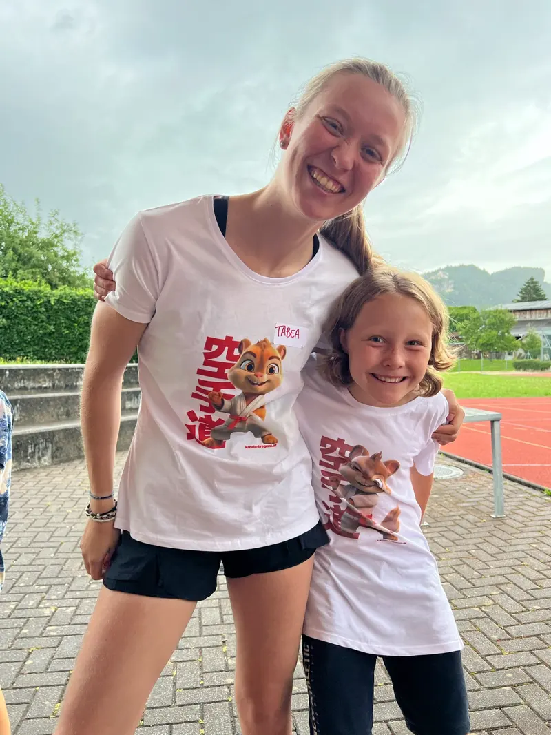 Betreuer und Kind tragen T-Shirts mit Karate-Schriftzeichen