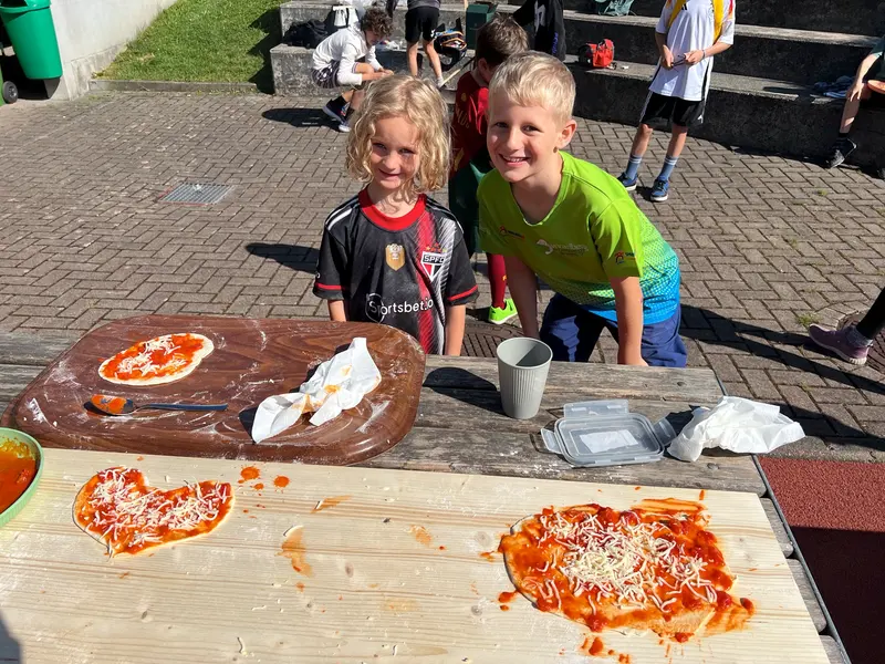 Zwei Kinder stehen an einem Tisch mit Pizzateig