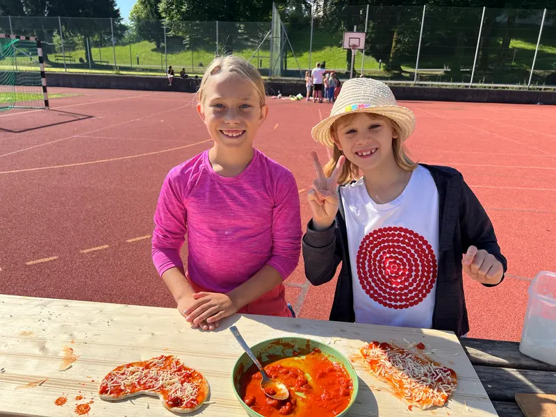 Zwei Kinder bereiten lächelnd Pizza an einem Tisch zu