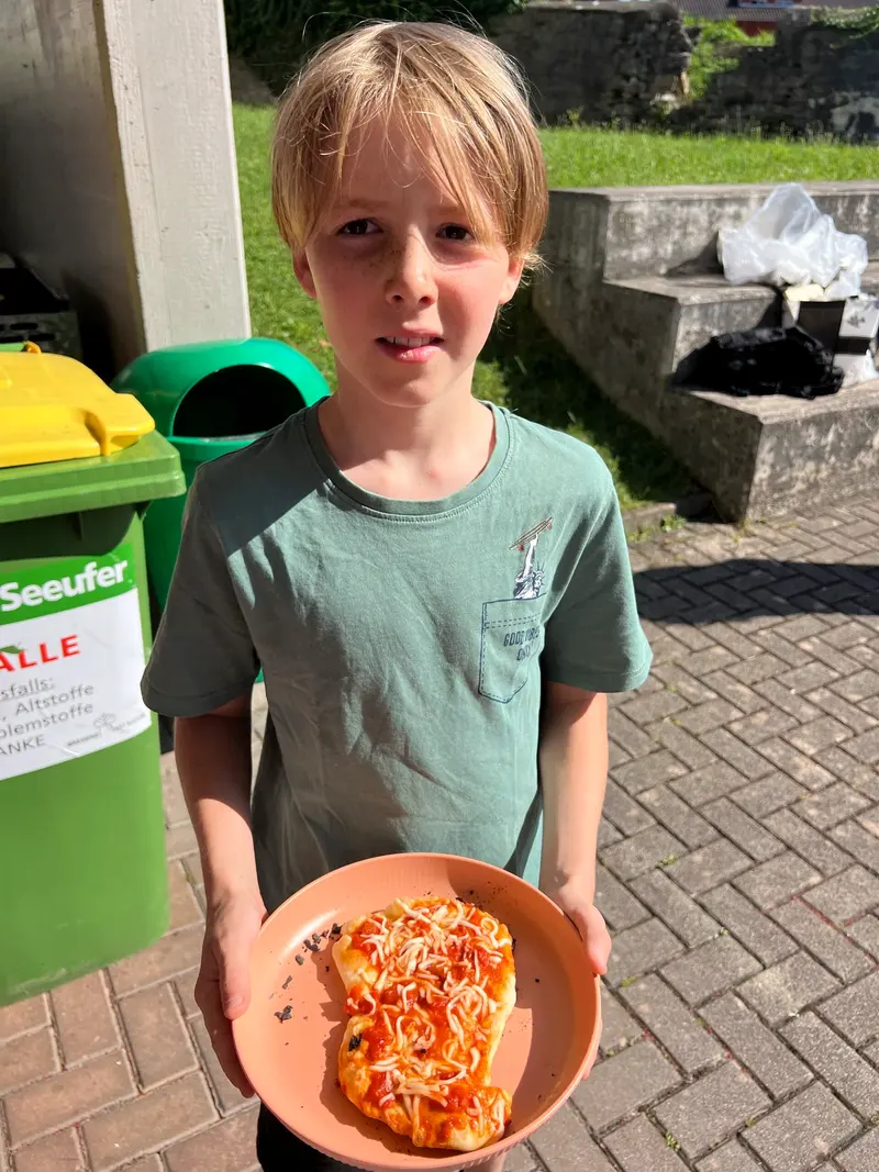 Kind hält einen Teller mit Essen neben Mülltonnen