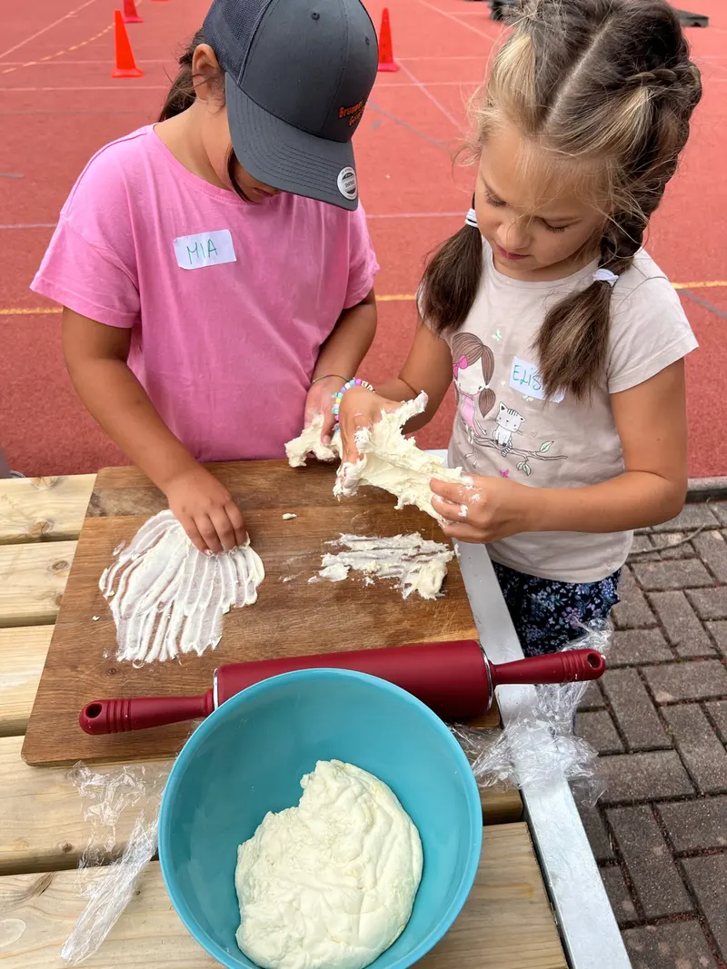 Zwei Kinder kneten Teig an einem Tisch im Freien