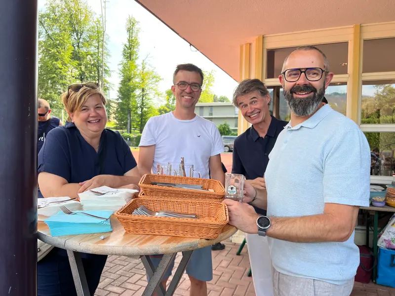 Gruppe sitzt gemeinsam an einem Tisch unter einem Vordach.