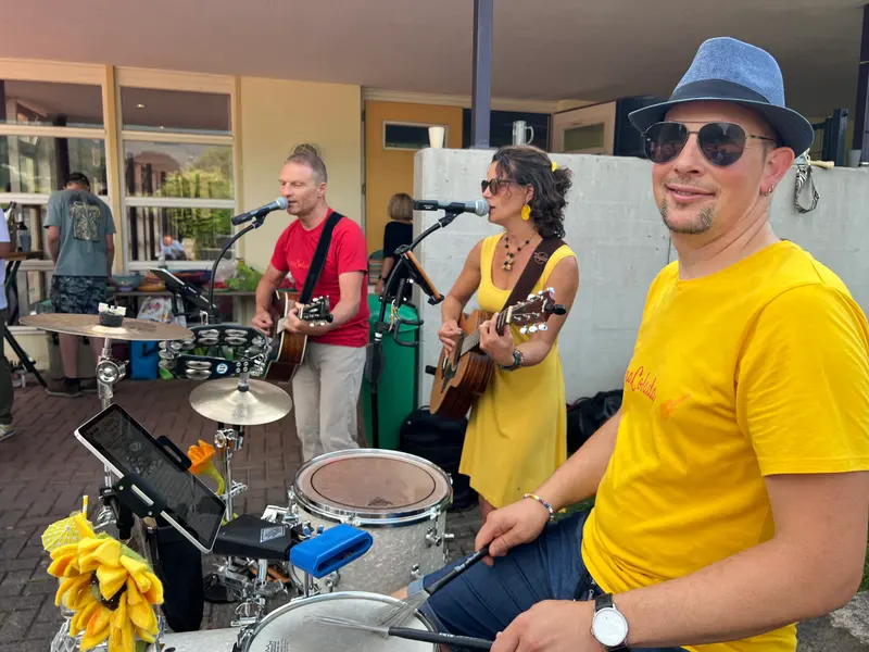 Musiker spielt Schlagzeug neben zwei Gitarristen im Freien.