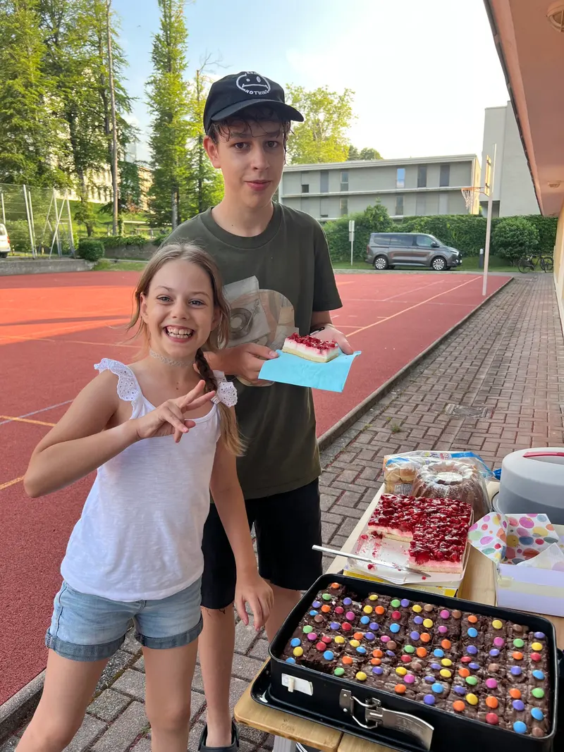 Kind zeigt lächelnd ein Victory-Zeichen auf einem Sportplatz.