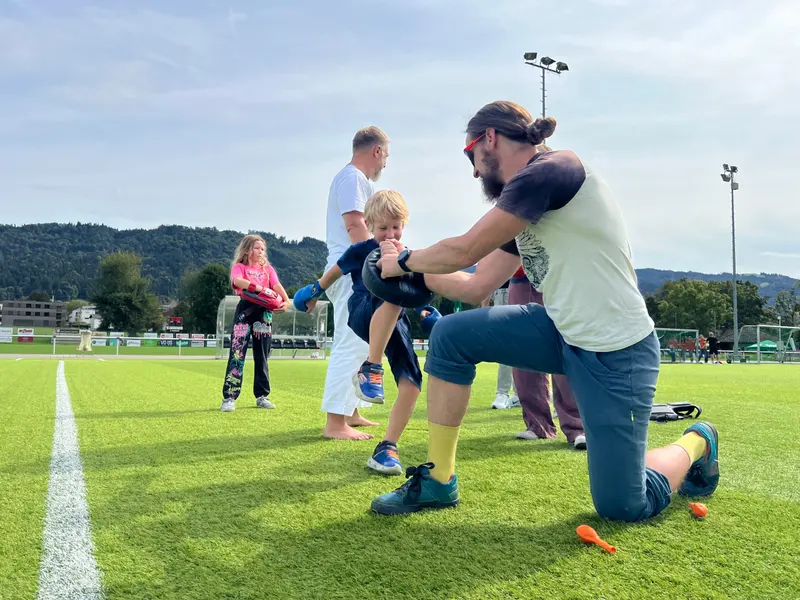 Trainer kniet auf Rasen und trainiert mit Kind