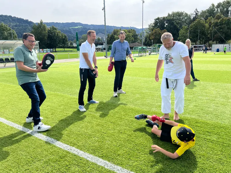 Gruppe steht im Kreis, Kind liegt am Boden