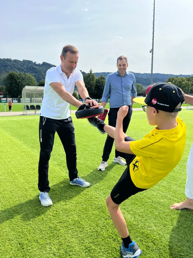Trainer hält Schlagpolster, Kind mit Kappe tritt dagegen