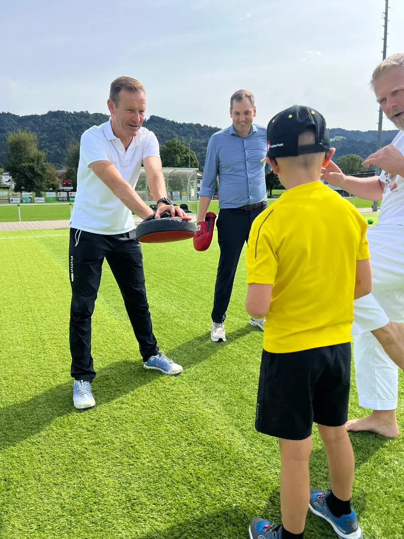 Trainer hält Schlagpolster für Kind im gelben Trikot