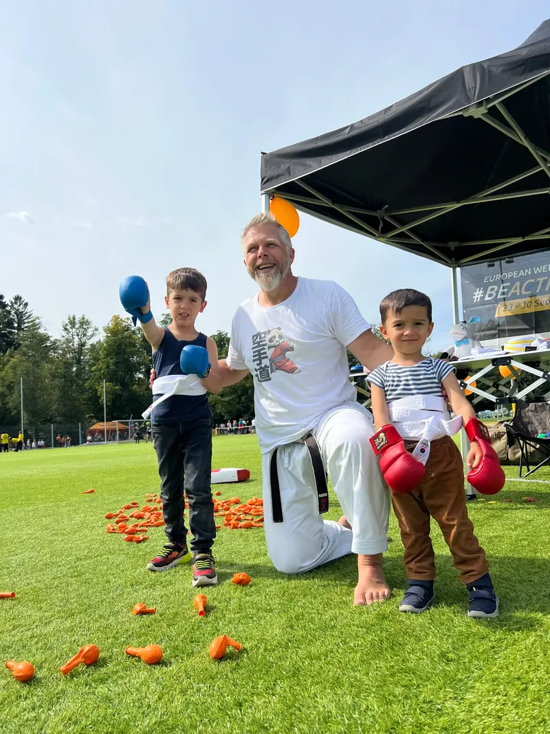 Trainer kniet zwischen zwei Kindern mit Boxhandschuhen