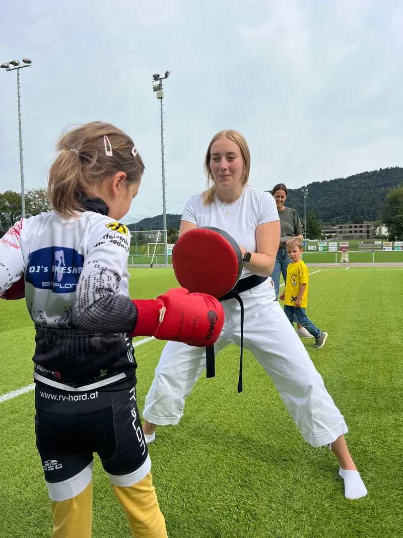 Zwei Personen trainieren mit rotem Schlagpolster auf Sportplatz