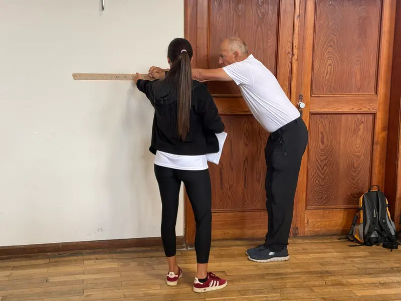 Zwei Personen üben eine Balanceübung mit einem Stab an der Wand
