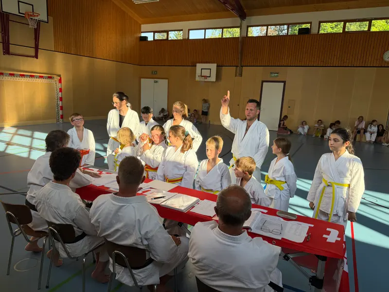 Gruppe sitzt vor dem Tisch, Trainer spricht mit erhobener Hand