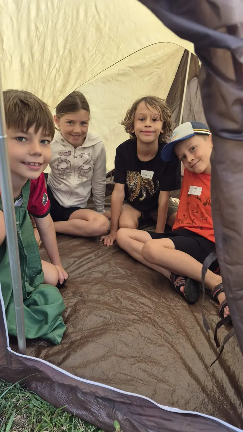Vier Kinder sitzen lächelnd in einem Zelt