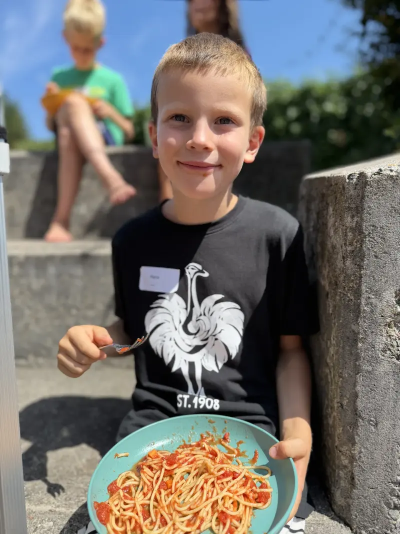 Kind sitzt auf Treppe und isst Spaghetti