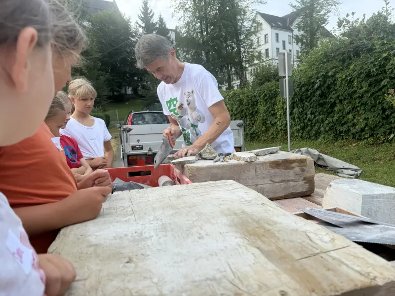 Kinder beobachten einen Mann beim Sägen eines Steins