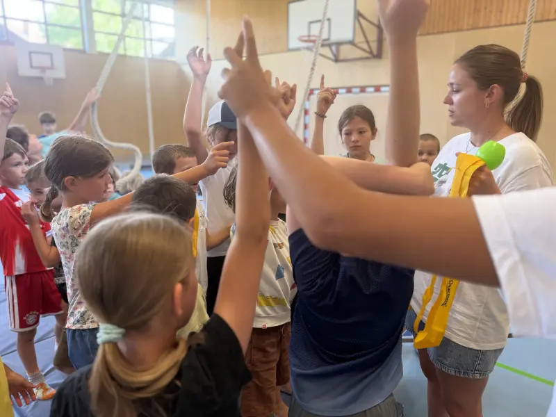 Kinder heben in der Sporthalle gemeinsam die Hände