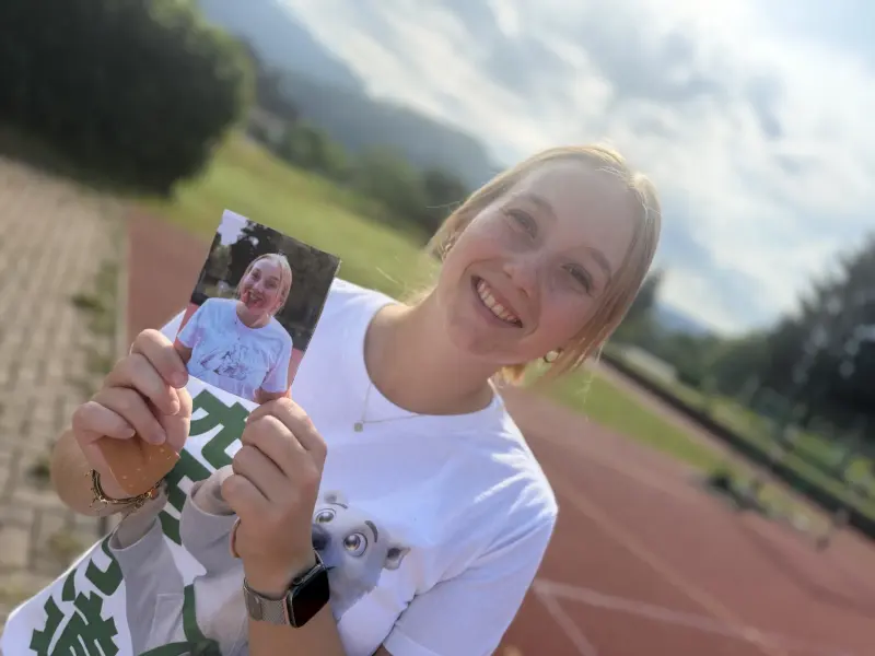 Person hält lächelnd ein ausgedrucktes Foto hoch
