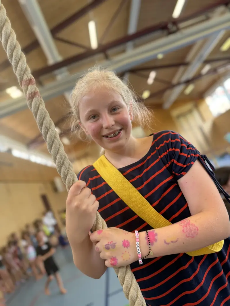 Kind hält lächelnd ein dickes Kletterseil in der Halle