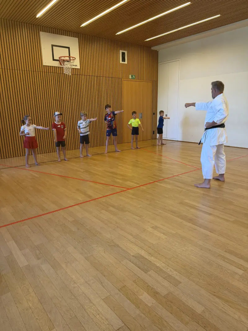 Karatelehrer zeigt Kindern eine Schlagtechnik in der Sporthalle