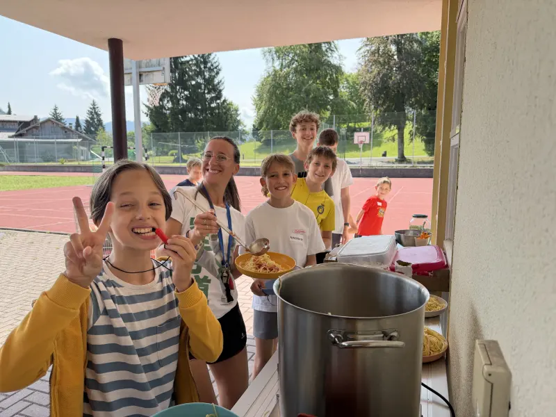 Kinder und Betreuerin servieren Spaghetti im Freien
