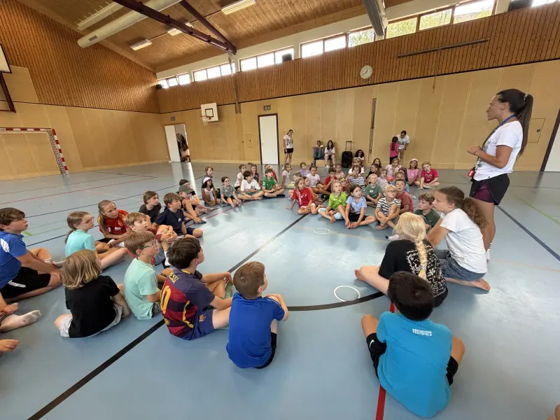 Große Gruppe Kinder sitzt im Kreis in der Sporthalle