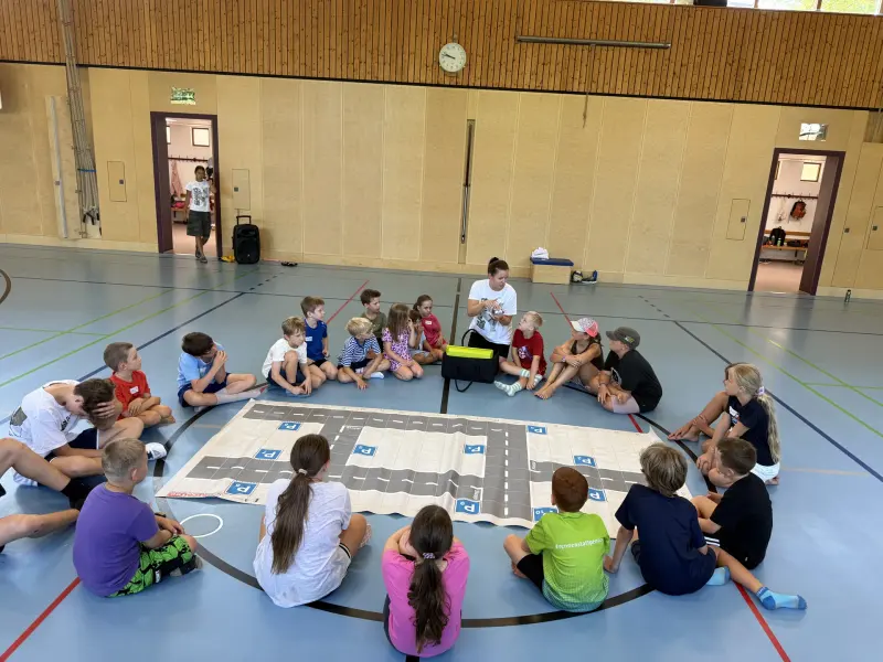 Kinder sitzen im Kreis um eine Spielmatte mit Straßenmuster