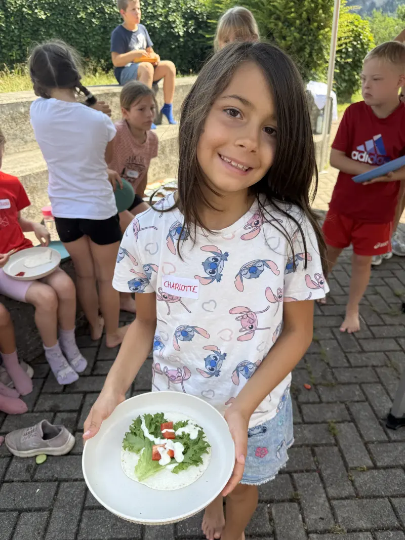 Kind zeigt Teller mit Wrap, Salat und Tomate