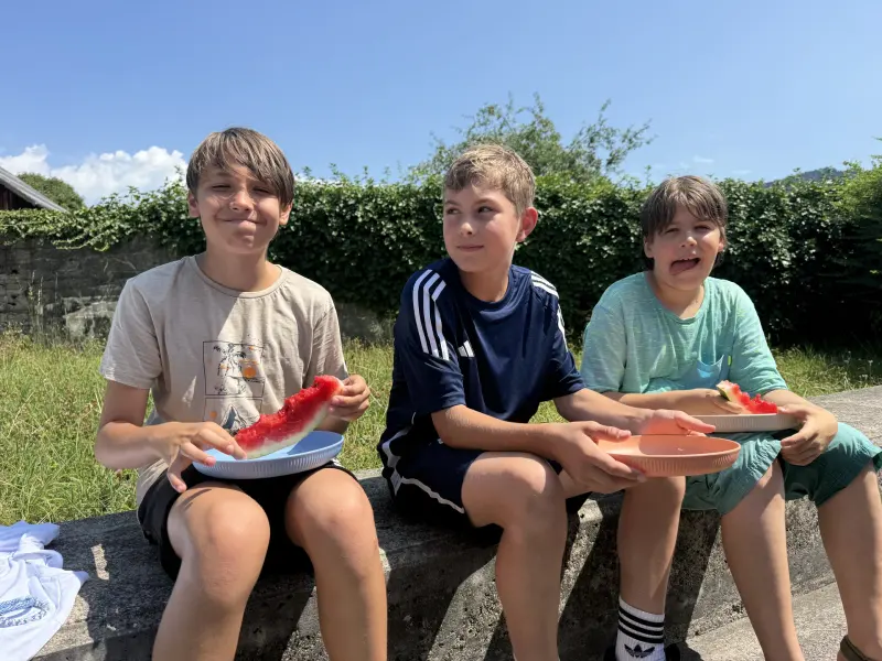 Drei Kinder sitzen auf einer Mauer und essen Wassermelone