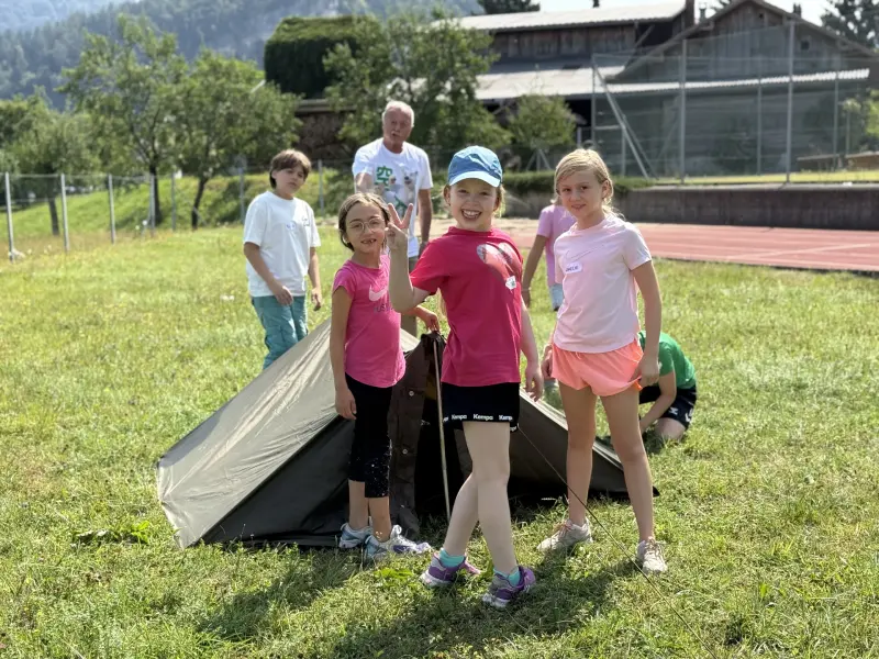 Kinder stehen vor aufgebautem Zelt auf einer Wiese