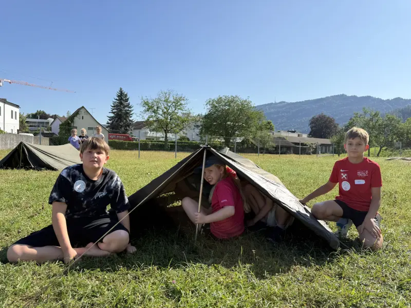 Kinder sitzen in selbstgebautem Unterschlupf auf der Wiese