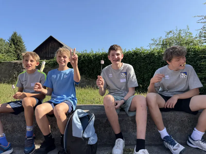 Kinder sitzen auf einer Mauer und essen Marshmallows