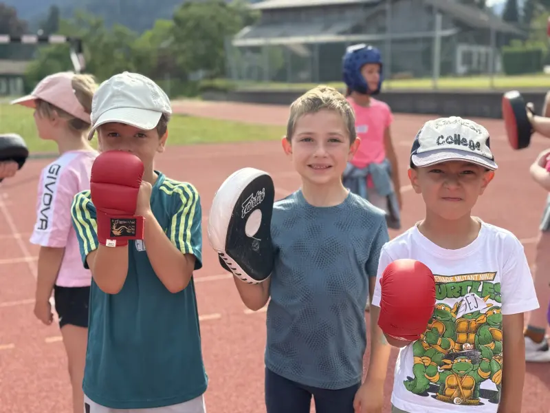Kinder trainieren mit Boxhandschuhen und Schlagpolstern im Freien