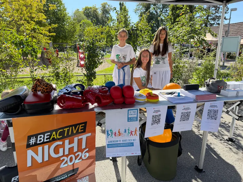 Stand von Karate Bregenz mit Karateausrüstung auf dem Tisch, dahinter zwei Jugendliche und eine Trainerin